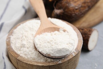 Wooden bowl and spoon with cassava flour on grey table, closeup