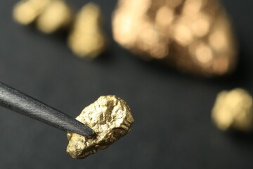 Tweezer with shiny gold nugget on blurred background, closeup. Space for text