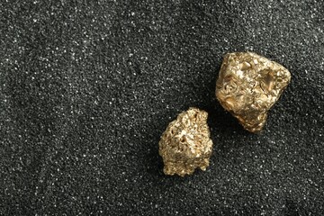 Shiny gold nuggets on black sand, top view. Space for text