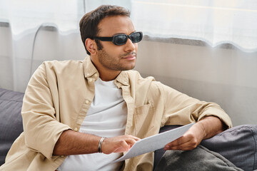 good looking indian man with blindness in cozy outfit sitting and reading braille code at home