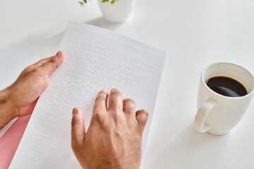 cropped view of indian man with blindness in casual attire with coffee reading braille code