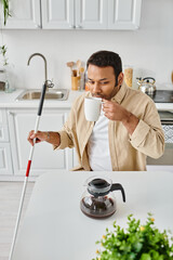 handsome indian man with visual impairment sitting and drinking tasty coffee while on kitchen
