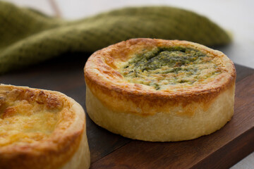 spinach and cheese quiche on a dark wooden board, with a green cloth for production and rustic white wooden background, horizontal photography, focus on spinach quiche