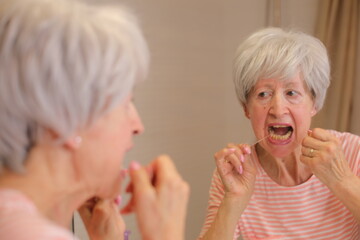Senior woman presenting difficulties to floss her teeth