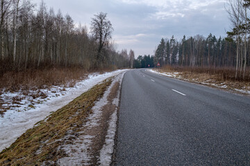 Obraz na płótnie Canvas Clean winter road in forest with turns and curve with trees. Winter road with white dividing line at winter season. Melting dirty snow on road side.