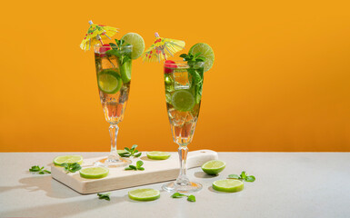 Two cocktails in long glass filled with ice and lemon slices garnished with small yellow umbrellas, cherries and lemon slices on a wooden board