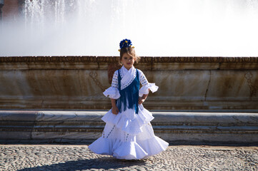 A pretty little girl dancing flamenco dressed in a white dress with ruffles and blue fringes in a...