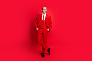 Full length photo of elegant young male cheerful smile hands pockets posing wear trendy classic garment isolated on red color background