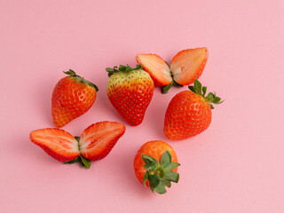 Strawberries cut in half and whole on a pink background. Strawberries close up.