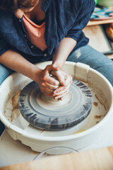 A young brunette potter at a potter's wheel. A middle-aged woman potter begins to shape a clay product on a potter's wheel in a bright workshop