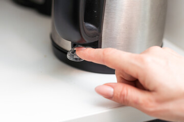 Woman's finger pressing the power switch on the electric kettle. Selective focus. Copy space is on...