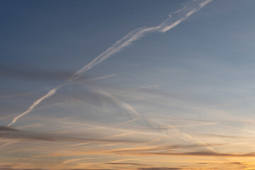 Paris, France - 01 28 2024: Sky Background. Detail view of a blue sky with colored clouds and aircraft trail at sunrise.