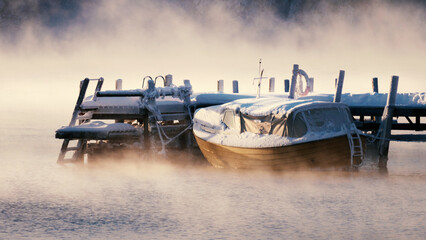 Small motorboat floating on the water in the frosty mist.