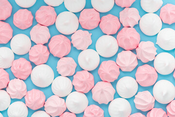 pink and white sweet meringue kiss cookies over blue background, flat lay, top view