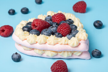 Pavlova meringue cake decorated with fresh raspberry and blueberry berries on blue background, close up