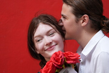 couple young man and woman hugging and holding the red bouquet rose flowers at red wall background. Concept couple life with love and happy moment.