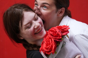 couple young man and woman hugging and holding the red bouquet rose flowers at red wall background....