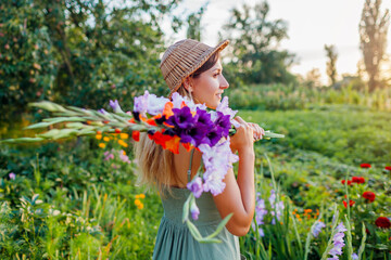 Portrait of young woman gardener holding bunch of fresh gladiolus in summer garden. Farmer picked...