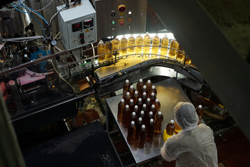 High angle of young staff in protective workwear bending over large metallic table with group of bottled soda or lemonade