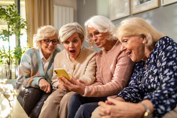 Senior women using a smartphone while sitting on a couch at home