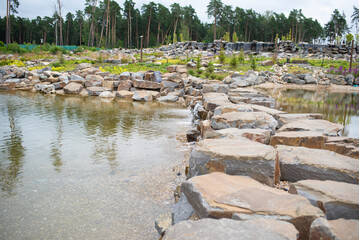 artificial waterfall, stones, pine trees in cloudy weather in summer. Odintsovo district, Moscow...