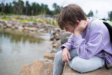 A 10 year old boy is resting, sitting on stones in a mountain park