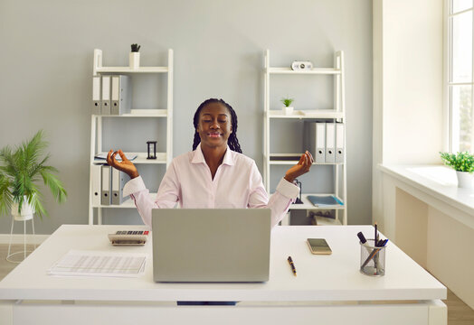 Business woman, corporate company worker, secretary or financial accountant doing stress relieving practices at work. Beautiful relaxed African American girl sitting at office desk and meditating