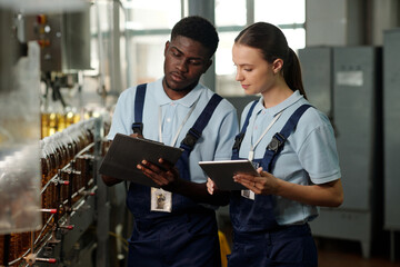 Young African American male engineer of quality control and his colleague with tablet checking...