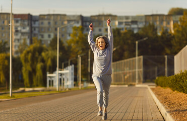 Fototapeta na wymiar Positive senior woman running and jogging with a smile in a city park. This dynamic scene captures the blend of happiness and sport, showcasing the woman enthusiasm for an active lifestyle.