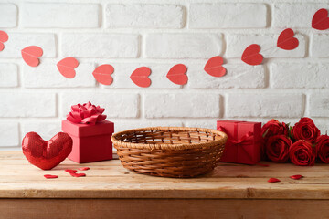 Empty basket on wooden table with gift box and heart shape garland over brick wall background. ...