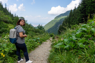 Naklejka na ściany i meble Female traveler walking along a forest path in the mountains