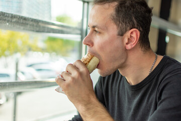 Man eating meat wrapped in pita bread and looking out the window
