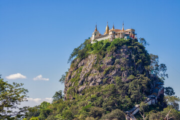 Mount Popa with numerous golden nat temples on the mountain with a sunny sky