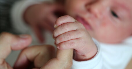 Cute newborn baby hand holding to father finger. Dad supporting infant newborn