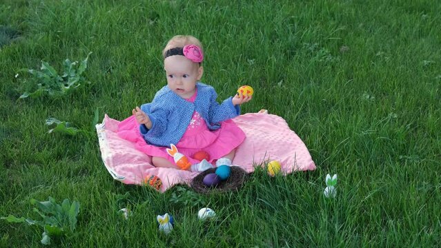 Cute baby girl playing with colorful Easter eggs while sitting on grass. Easter hunt concept