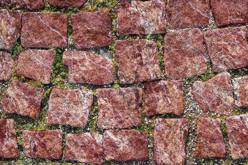 Texture of paved stone road with sprouted grass between masonry.