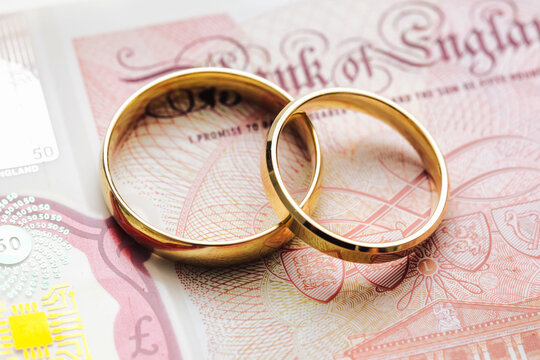 Wedding rings on money. Cost of wedding. Price of getting married background. Golden jewelry on banknote. Cash for getting divorced. Expensive marriage. Fifty pound note.