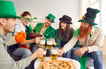 Happy Saint Patrick day friend home party, celebration of national Irish culture with pizza, beer. Group of fancy dressed people with Irish drink, wearing silly green hat, beard, social entertainment - obrazy, fototapety, plakaty