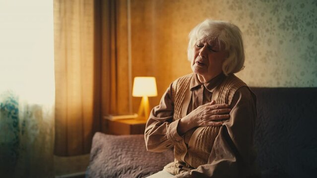 Elderly woman suffering from strong chest pain at home, risk of heart failure