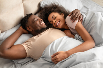 black man and woman lying in bed hugging radiating happiness