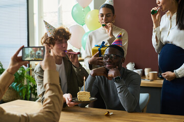 Happy young African American man sitting by table among his intercultural colleagues congratulating him on birthday