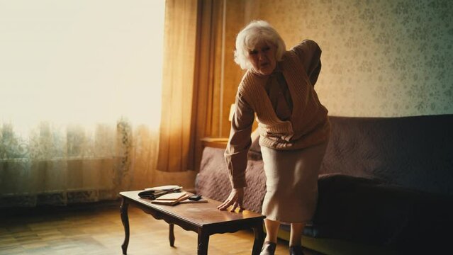 Elderly woman suffering from sharp back pain while standing up from sofa