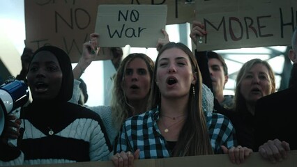 Multiracial woman with megaphone in protest with diverse group activist people who demonstrate together shouting slogans against wars in world asking with banners for peace, love, hugs and not armies