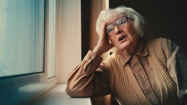 Unhappy elderly woman looking out the window, remembering past life, melancholy