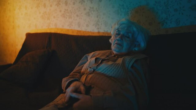 Old woman wearing nasal cannula fell asleep on sofa while watching tv at night