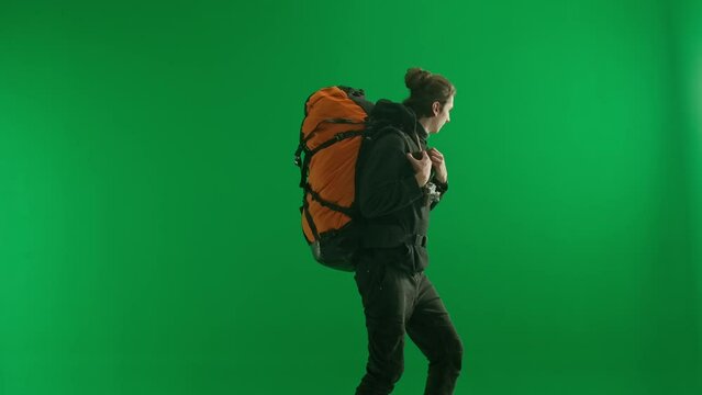 A male traveler with a backpack on his back and a retro camera around his neck climbs up on a green screen close up. After reaching the top, the happy man takes photos with the retro camera.