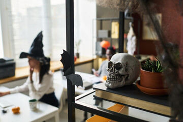 Human skull and flowerpot with green domestic plant standing on book on shelf against young...