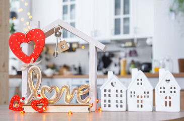 Key to tiny house of cozy home with Valentine decor on table of kitchen. Gift for valentines day, family love nest. design, project, moving to new house, mortgage, rent and purchase real estate