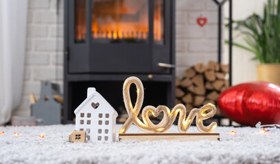 Key to house with keychain against background of fireplace stove with fire and firewood in Valentine decor, love home. Moving to new house, mortgage, rent and purchase real estate