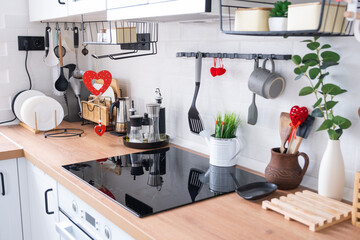 The interior of the kitchen in the house is decorated with red hearts for Valentine's Day. Decor on the table, stove, utensils, festive mood in a family nest